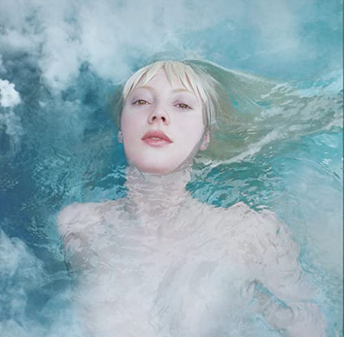 Woman with blonde hair floating in blue water, face forward.