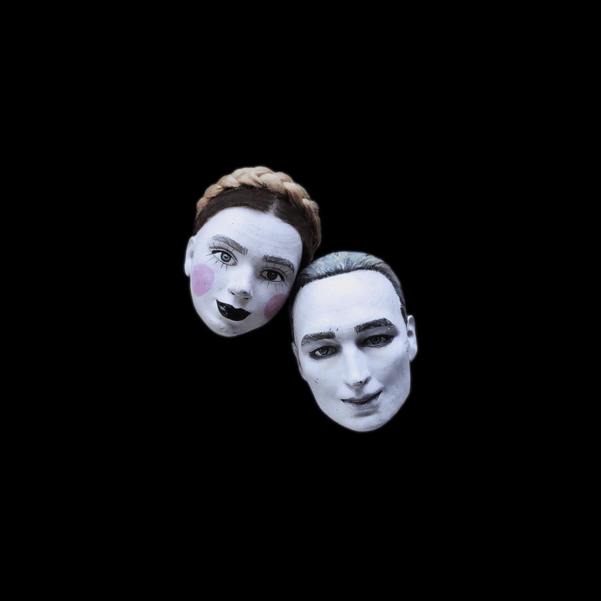 Two pale-faced figures with stylized makeup against a black background.