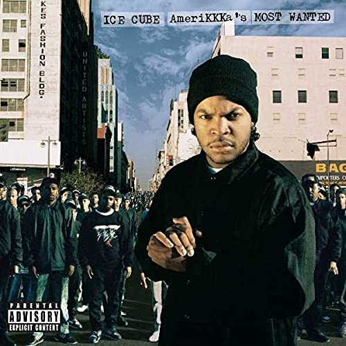 Ice Cube wearing a black beanie and jacket, standing before a crowd in city.