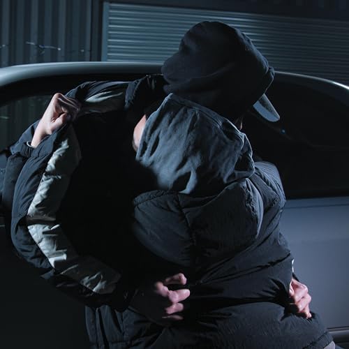 Two hooded figures embrace near a dark car, album cover art.