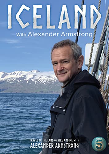Alexander Armstrong on a boat with snowy mountains and ocean in the background.