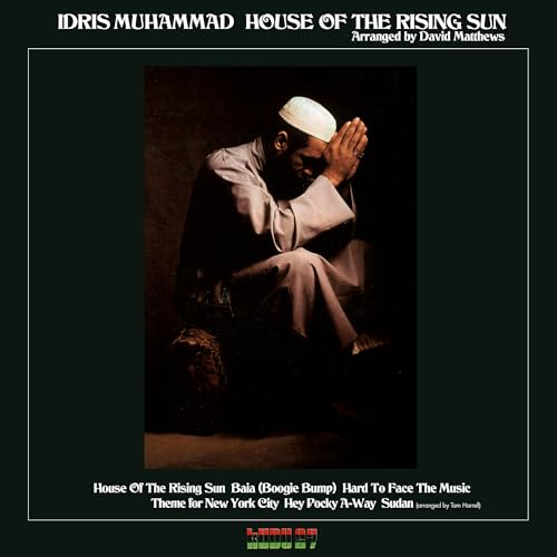 Idris Muhammad wearing a prayer cap with hands clasped against a dark background.