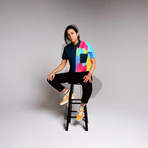 Woman sitting on stool, wearing colorful shirt and black pants.