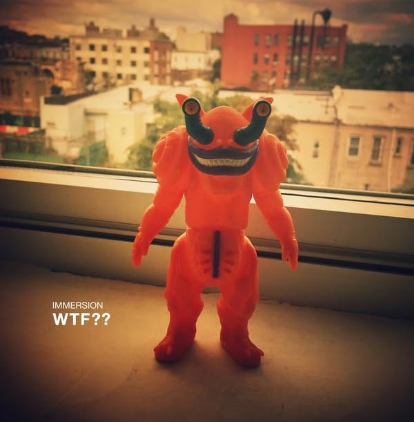 Orange monster toy stands on a windowsill with a city backdrop.
