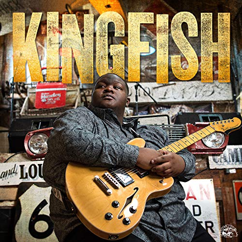 Christone Kingfish Ingram holding a hollow-body electric guitar against a rustic, textured background.
