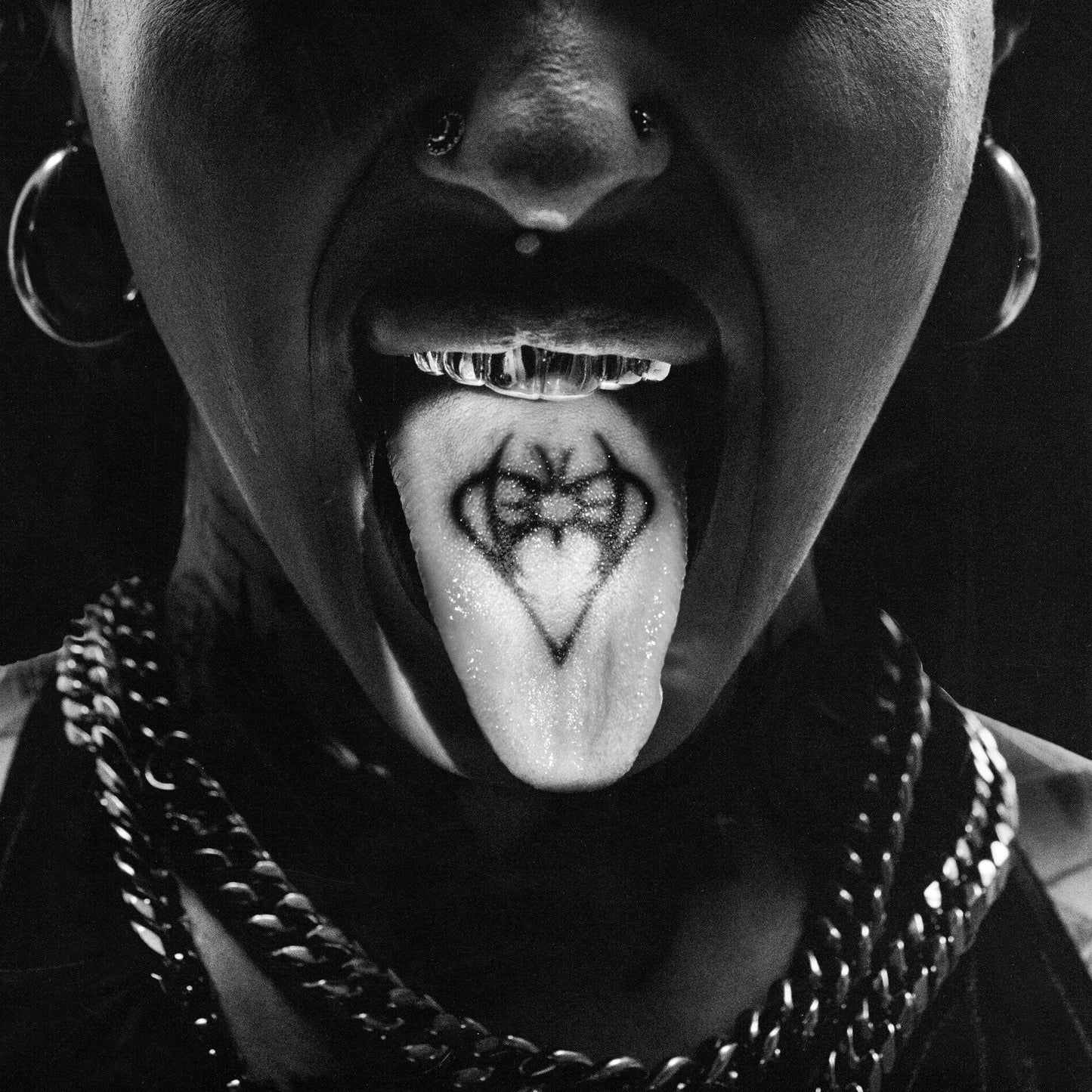 Black and white close-up of a person with a tongue tattoo and piercings.