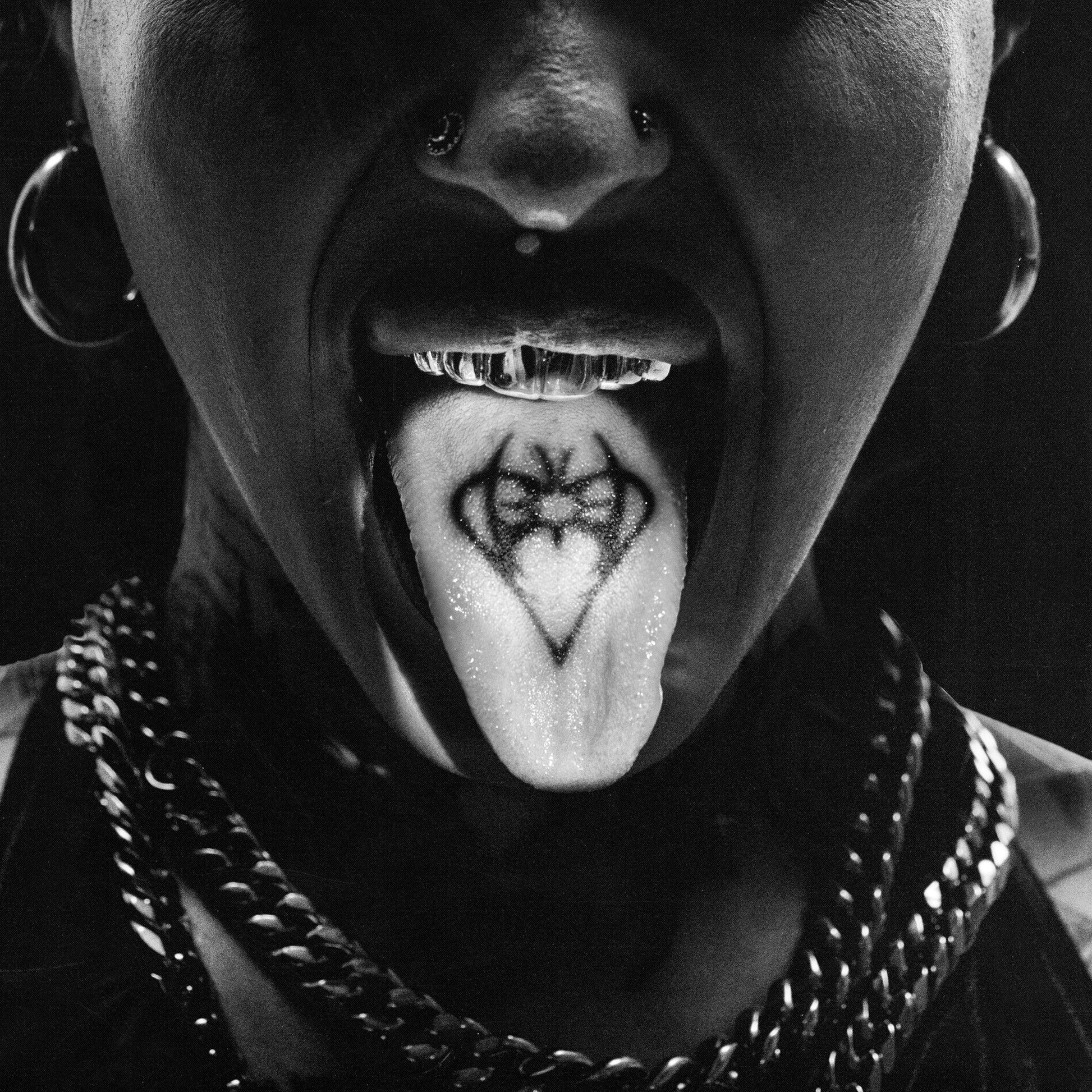 Black and white close-up of a person with a tongue tattoo and piercings.
