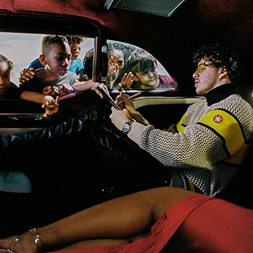 Jack Harlow sitting in a car writing while children look through the window.