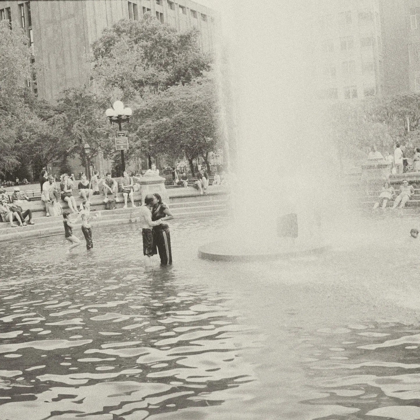 Black and white photo of people in a city park fountain with a large spray.
