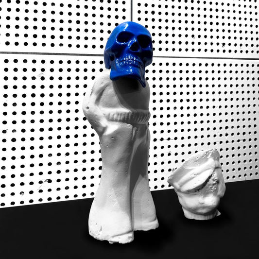 Blue skull sculpture on a white bust, against a dotted wall.