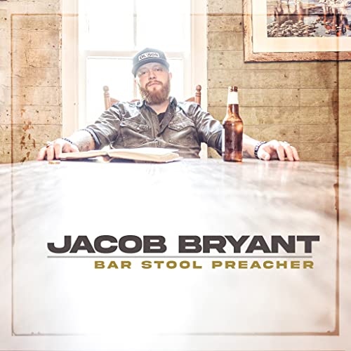 Bearded man at a table with a beer and open book.