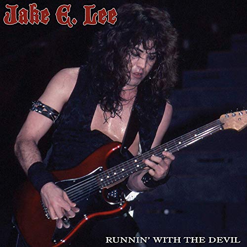 Jake E. Lee with long hair playing an electric guitar on stage.
