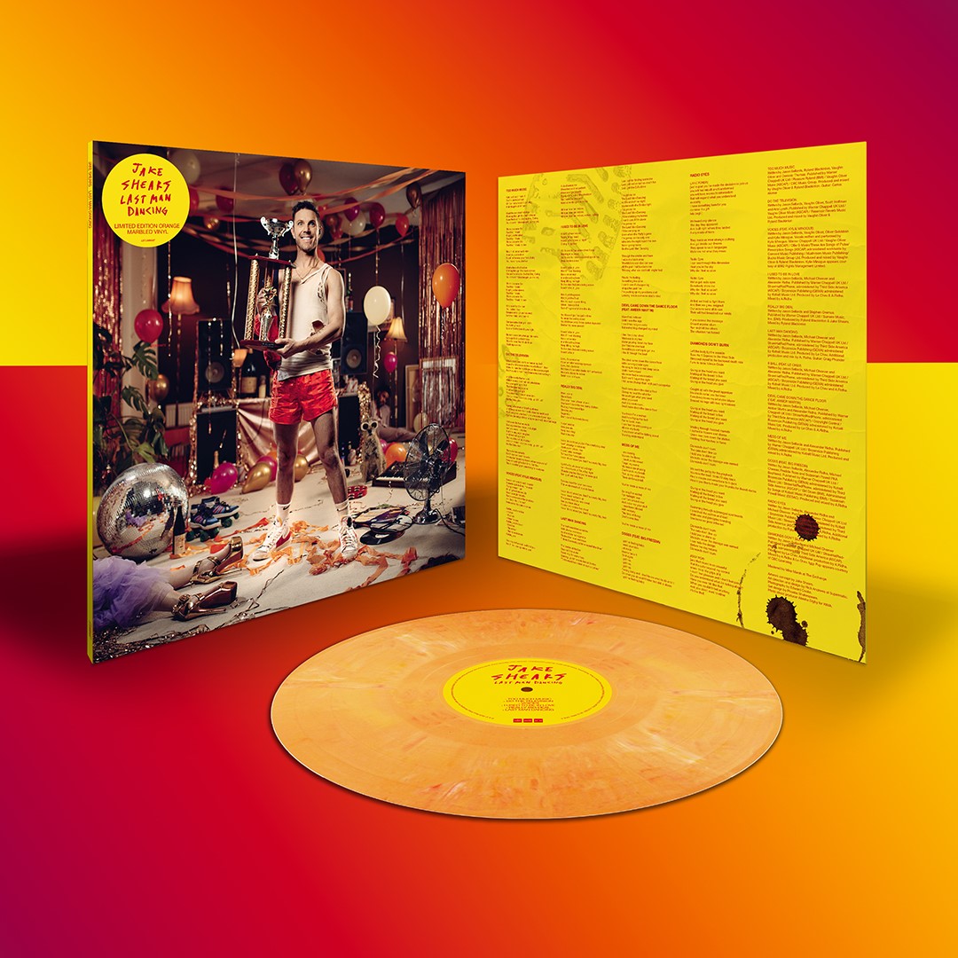 "Orange vinyl record with album cover featuring a man holding a trophy amidst party decorations."