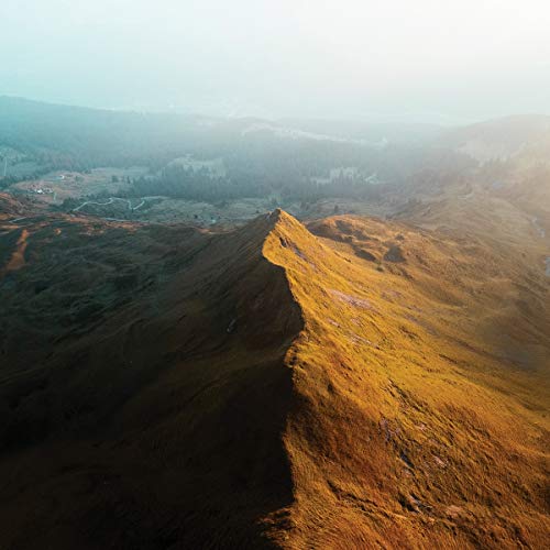 Aerial view of a golden, rocky mountain ridge under a hazy sky.