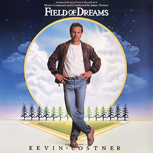 Kevin Costner stands in a baseball field with cornstalks against a starry night sky.