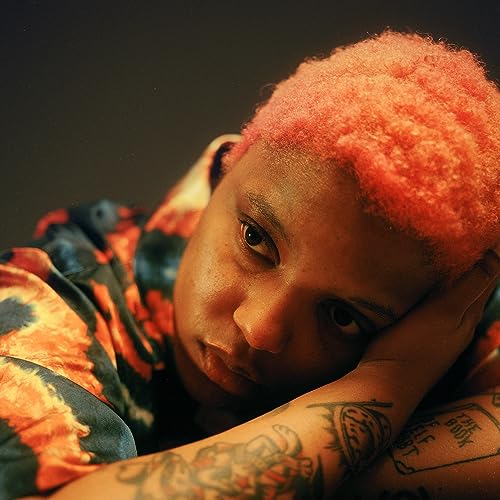 Loraine James with short, coral-colored hair and visible arm tattoos.