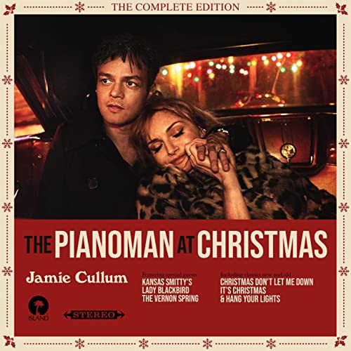Jamie Cullum and a woman sitting in a car with Christmas lights in background.