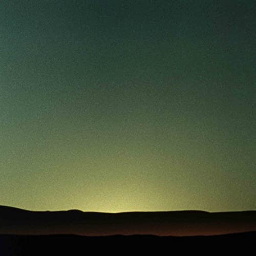 A grainy, dark landscape silhouette against a glowing, pale green twilight sky.