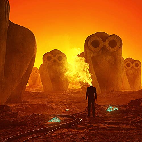Man facing large owl statues with a fiery, orange background.