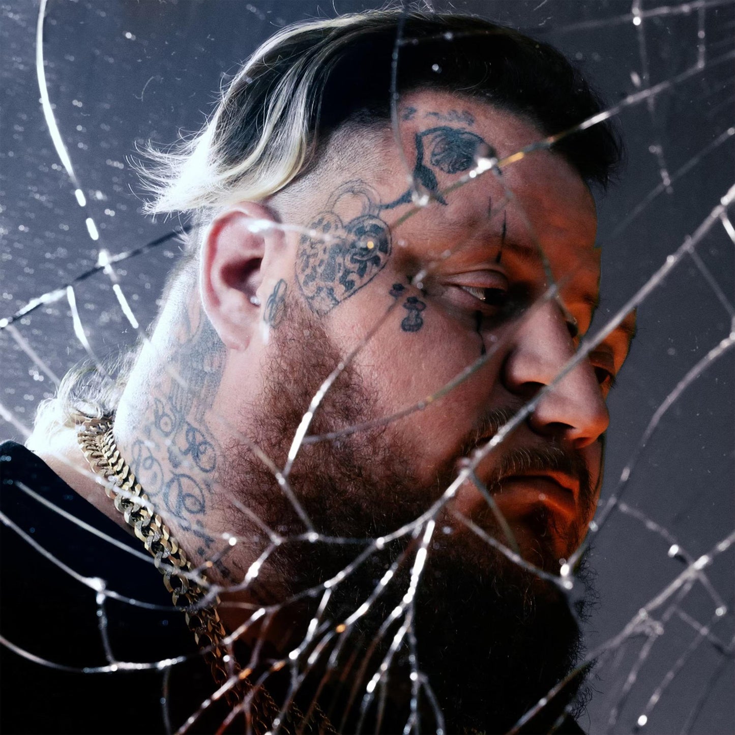 Jelly Roll with face tattoos viewed through a cracked glass surface.