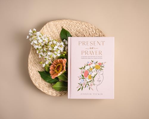 Pink book, “Present in Prayer”, rests on a woven tray with flowers.
