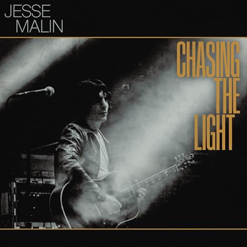 Jesse Malin plays an acoustic guitar on stage in a smoky, black and white photo.