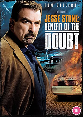 Tom Selleck in a brown jacket with a burning police car and house behind.