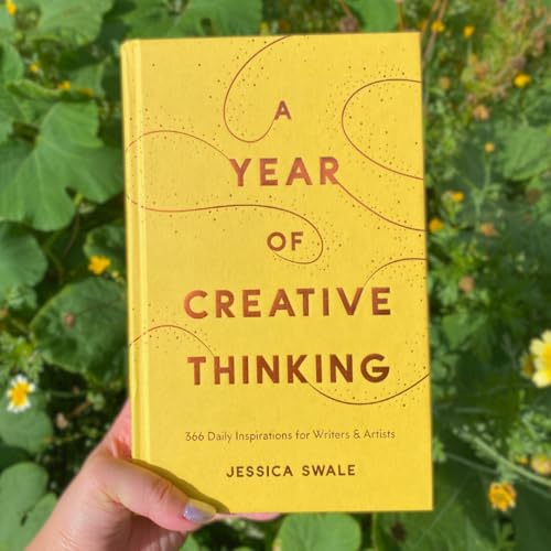 Yellow book, “A Year of Creative Thinking,” held against green foliage.