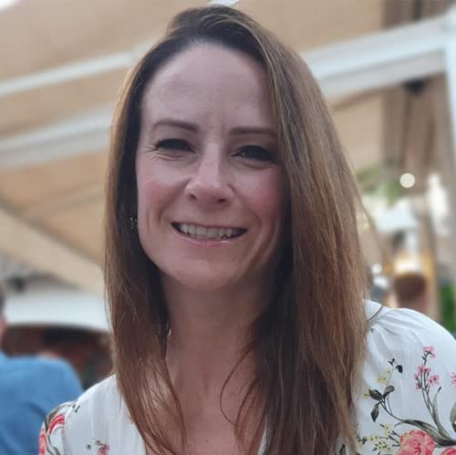 Woman with brown hair smiling, book cover partially visible behind her.