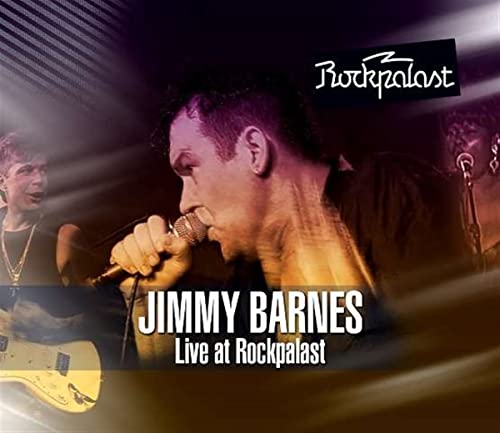 Jimmy Barnes singing into a microphone on stage with band members in the background.