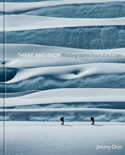 Two people with backpacks walk across a vast, snowy landscape with layered blue ice formations.