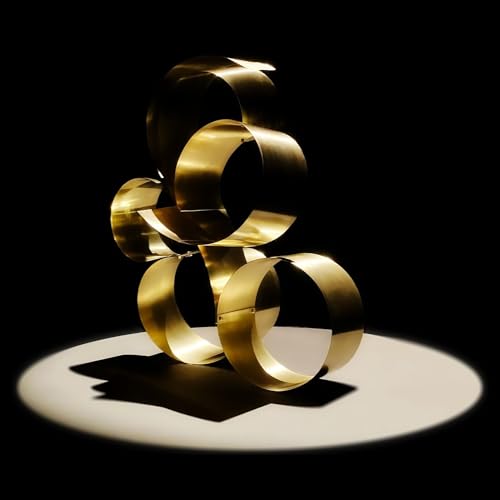 Golden, circular sculpture on a white surface with dramatic lighting.