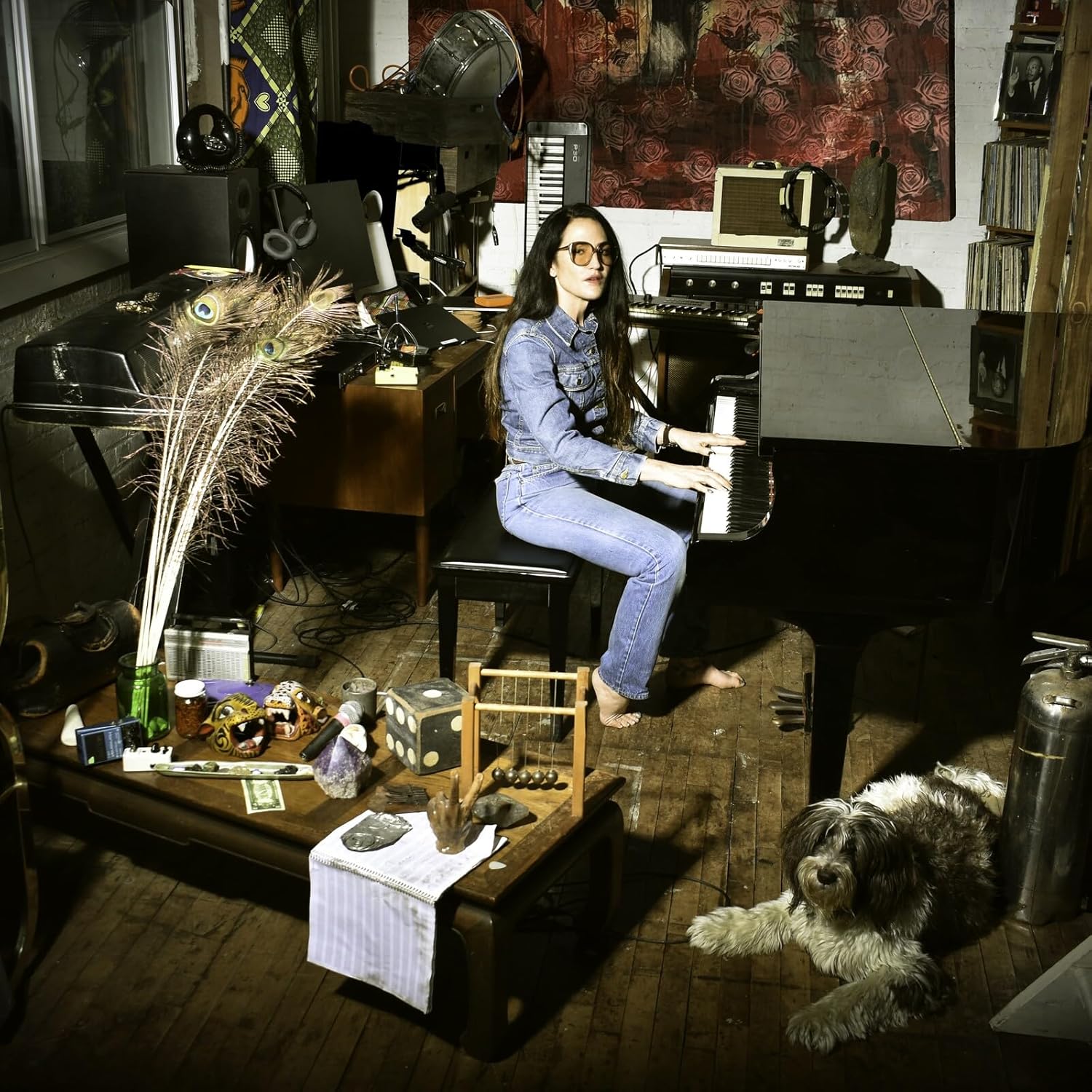 Joan Wasser plays a grand piano in a cluttered studio with a shaggy dog.