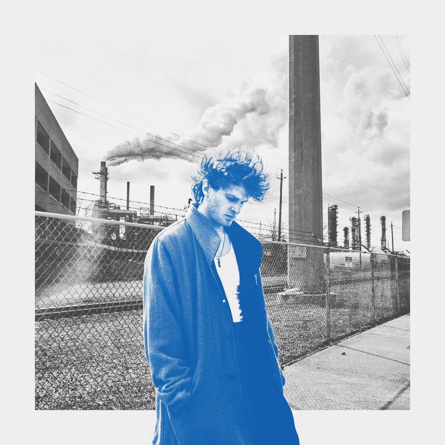 Man in blue coat stands before an industrial landscape.