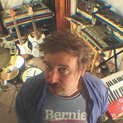 Man with curly hair in front of musical instruments and equipment.