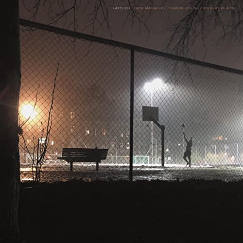 Nighttime park scene with a basketball hoop, bench, and lone figure.