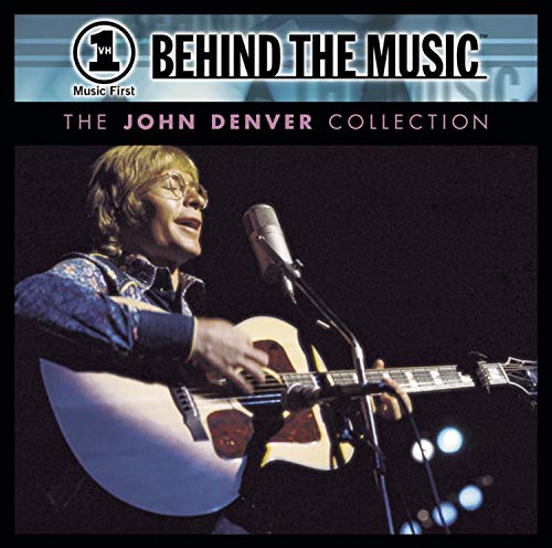 John Denver playing acoustic guitar and singing into a microphone on stage.