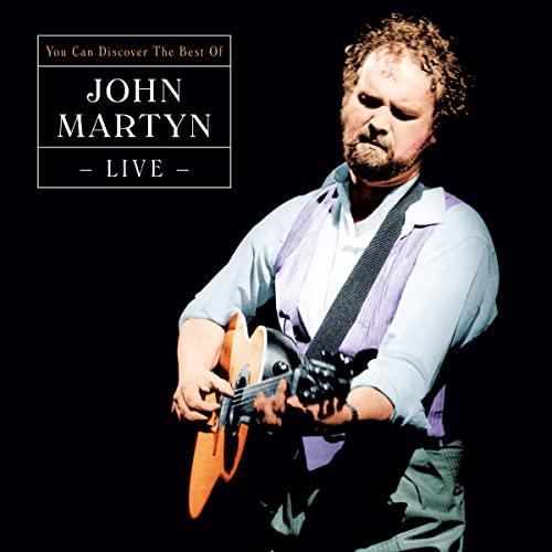 John Martyn playing acoustic guitar on stage against a black background.
