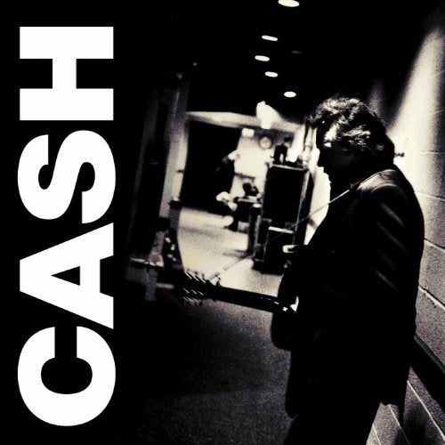 Johnny Cash stands in a dark hallway holding a guitar with the word CASH vertically.