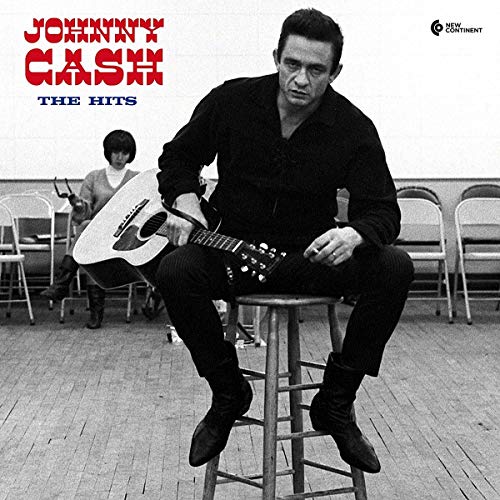 Johnny Cash sitting on a stool holding a guitar in a black and white photo.