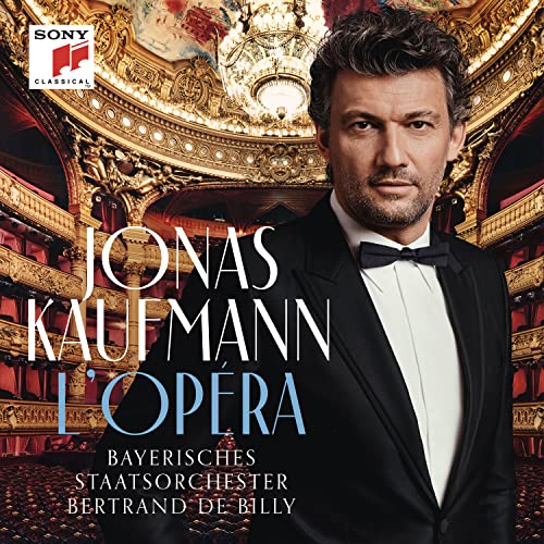 Jonas Kaufmann portrait in a tuxedo, standing in an ornate opera house.