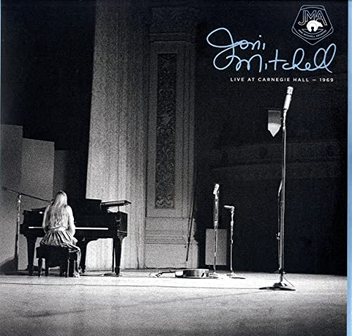 Joni Mitchell playing piano on stage at Carnegie Hall in a black and white photo.