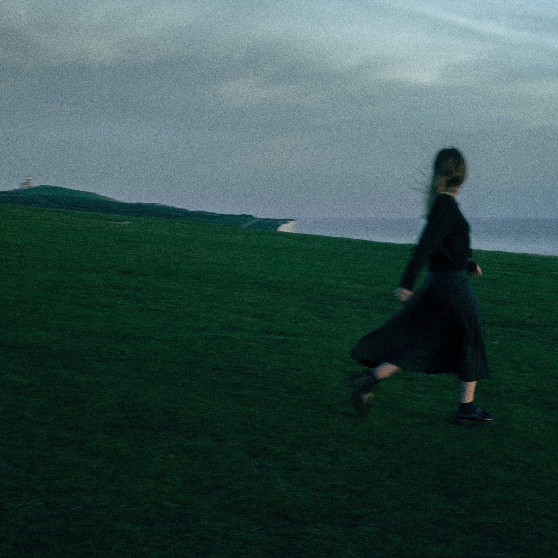 Blurred image of a woman running on a grassy hill by the sea.