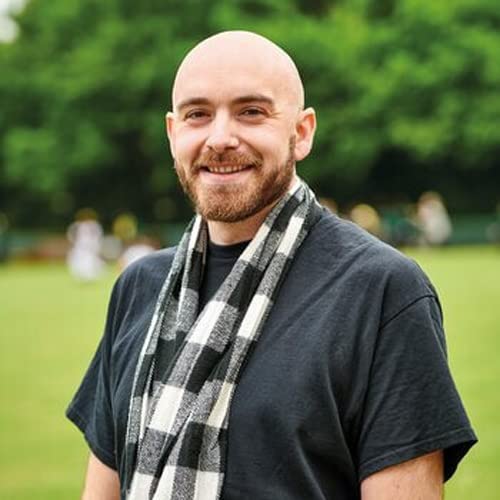 Man with a beard and scarf smiles at the camera outdoors.