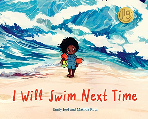 A young child with arm floaties stands on a beach before a large wave.