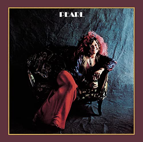Janis Joplin sitting on a chair with pink hair and red pants.