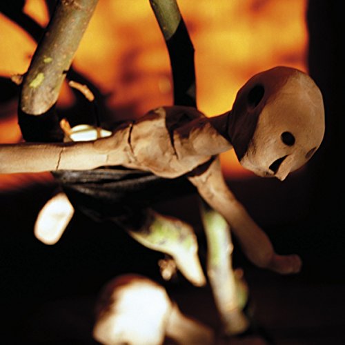 Wooden figure hanging from branches against a blurred orange background.