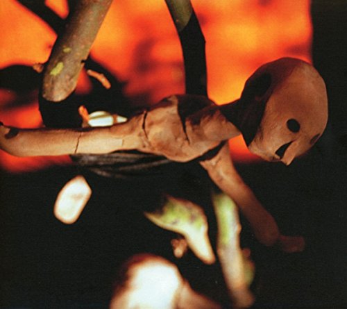 Wooden puppet figure with dark voids for eyes, against an orange background.