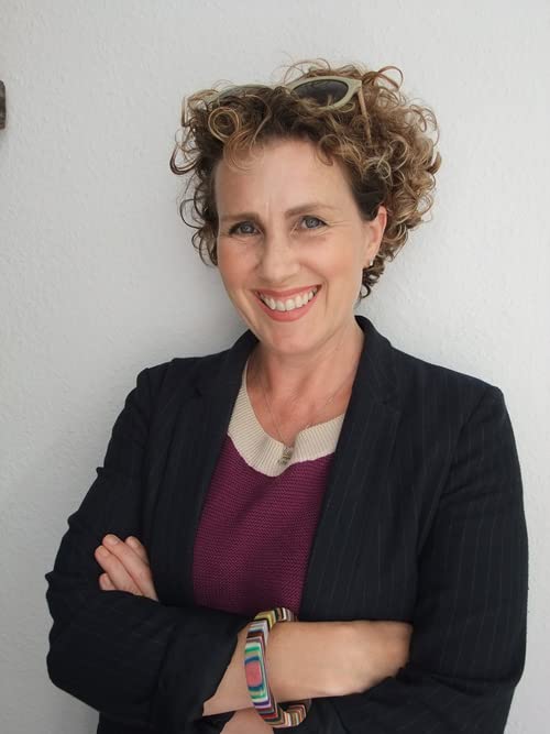 Woman with curly hair smiling, wearing a blazer and colorful bracelet.