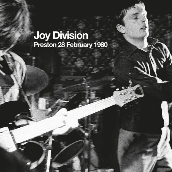 Black and white photo of Joy Division performing live on stage in 1980.